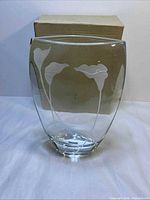 Front view of clear glass vase with frosted calla lilies and box behind