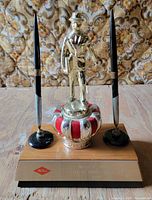 Front view of award showing salesman figure, crown, pens, brass plate
