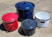 Four enamelware pots with lids displayed outdoors