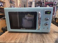 Front view showing aqua microwave with chrome handle, digital display, and knobs