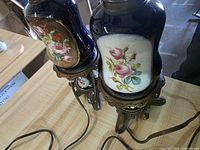 Both lamps showing porcelain bodies with floral panels and metal bases