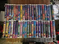 Full spread of approximately 35 Disney VHS tapes laid out spine-up on tabletop
