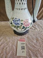 Close-up of lower body displaying blue and pink floral decoration and wood base