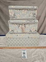 Three grey satin boxes stacked to show size variation and exterior patterns