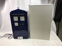 Front view of the TARDIS mini fridge with original box next to it, showing police box design and power cord.