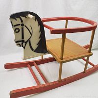 Side view of vintage wooden rocking horse showing painted horse head, red curved railings, and wooden seat and rockers.