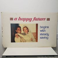 Front view of vintage bank poster showing couple and text 'a happy future begins with steady saving'.