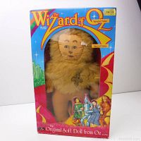 Front view of Cowardly Lion soft doll in original box with clear plastic window. Box shows Wizard of Oz branding and colorful artwork.