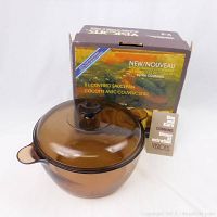 Full view of amber glass saucepan with matching lid, original box behind, and instruction sheet beside it.