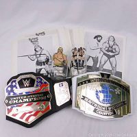 Overview of two replica championship belts, black and white, and black & white wrestling photos behind them.