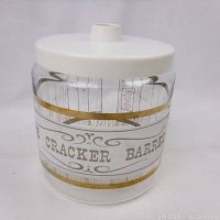 Front view of clear glass Pyrex cracker barrel storage jar with gold accents and white lid.