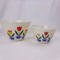Two white opaque glass bowls with colorful tulip pattern on the exterior sides, one larger and one smaller, standing side by side on white background.