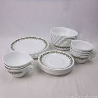 Full view of the dish set showing stacks of plates, bowls, and cups with green floral pattern on white background