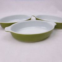 Three vintage Pyrex green oval mini casserole dishes arranged with edges touching, showing white interiors and green exteriors.