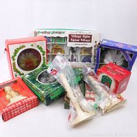 Overview of all vintage Christmas decorations including an Alpine village set, angel tree topper, bubble light, scented candle, electric candles, and bottle decorators. All items in original packaging.
