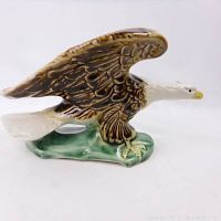 Side view of ceramic bald eagle planter with brown wings, white head, yellow beak and claws on green base