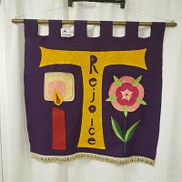Front view of vibrant purple felt banner depicting a yellow cross with "Rejoice" text, candle flame, and flower designs.
