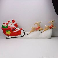 Full view showing Santa in sleigh with two reindeer in flying pose, sitting on white base representing snow.