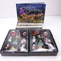 Two boxes containing a total of 18 assorted ceramic Christmas tree ornaments, displayed in original plastic trays, with bright colorful paint and holiday designs.