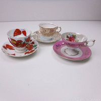 Three English tea cups and saucers arranged in a group, showing distinct floral patterns and gold trim.