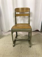 Front view of vintage school chair showing wooden seat and metal frame.