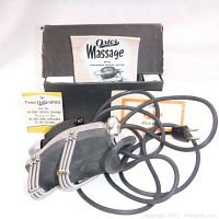Oster Stim-U-Lax Junior handheld electric massager with power cord and original instruction booklet inside the opened original box.