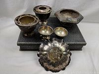 Silver pieces including flower dish, shrimp bowl, and pedestal containers placed on top of the silverware chest showing tarnish on surfaces.