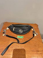 Full view of Guess black fanny pack with chain and adjustable strap laid flat on table