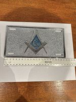 Front view of silver glitter plate with Masonic emblem and ruler for scale