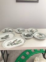 Seven porcelain plates and one platter on table showing fish motifs and crackle borders