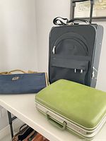 All three pieces on table: Bugatti suitcase upright, Samsonite case closed, Rolex garment bag folded