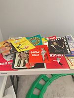 Assorted stack of approximately 15 vintage programs on table; visible Hello Dolly, The Monkees, Wildcat, unidentified titles