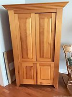 Front view of closed plywood entertainment cabinet with paneled doors and crown moulding