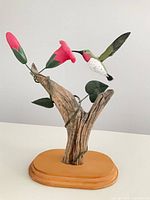 Front view of carved wood hummingbird feeding at flower on driftwood trunk and oval base
