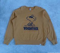 Full front view of mustard yellow Woodstock crewneck laid flat