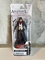 Front view of sealed Assassin’s Creed Arno Dorian action figure package showing figure and accessories