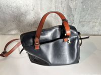 Front and side view of Fossil black leather handbag showing handles, strap and key charm