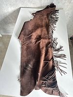 Full view of brown suede leather chaps laid flat showing length and fringe