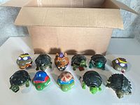 Line-up of 11 TMNT turtle figures in front of box