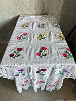 Blanket spread out showing overall pattern of crocheted squares and multicolour embroidered flowers