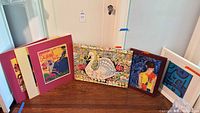 Front view of all six framed artworks leaning against wall