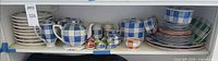 Shelf view showing plates, teapots, shakers, canisters, assorted dishes in checkerboard pattern