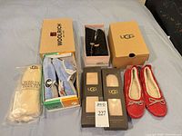 Overview showing UGG insoles packages, blue terry slides, red moccasins, Woolrich, UGG and other branded boxes