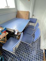 Table and chairs viewed from side angle showing blue laminate surface, chrome legs, four chairs