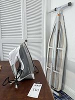 Side view of iron standing upright beside folded ironing board showing overall lot