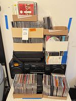 Stacked boxes of music CDs on top of Sony boombox and speakers