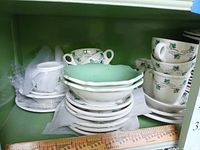Mixed Syracuse China patterns stacked on shelf showing plates, cups, green interior bowls