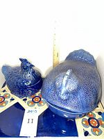 Large and small blue ceramic hen-shaped covered dishes side by side