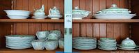 Full cabinet view showing stacks of plates, bowls, two covered tureens, platter, sugar bowl, creamer, butter dish