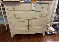 Front view of white serpentine chest showing drawers, doors, knobs and wear